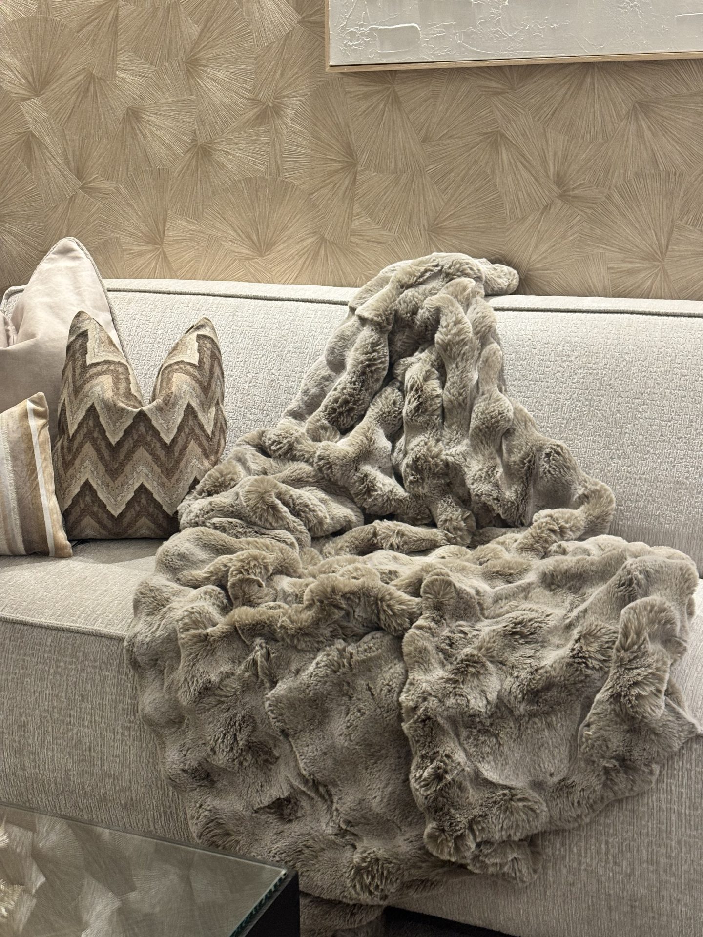 Fluffy taupe plaid over de hoek van een lichte bank met beige sierkussens