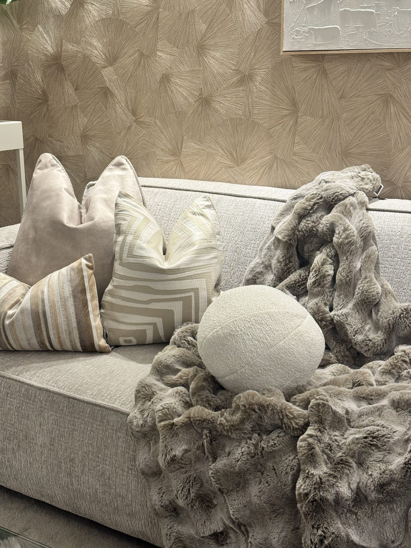 Zachte plaid in taupe die los over een lichte bank valt, met drie sierkussens in beige en zandtinten ernaast
