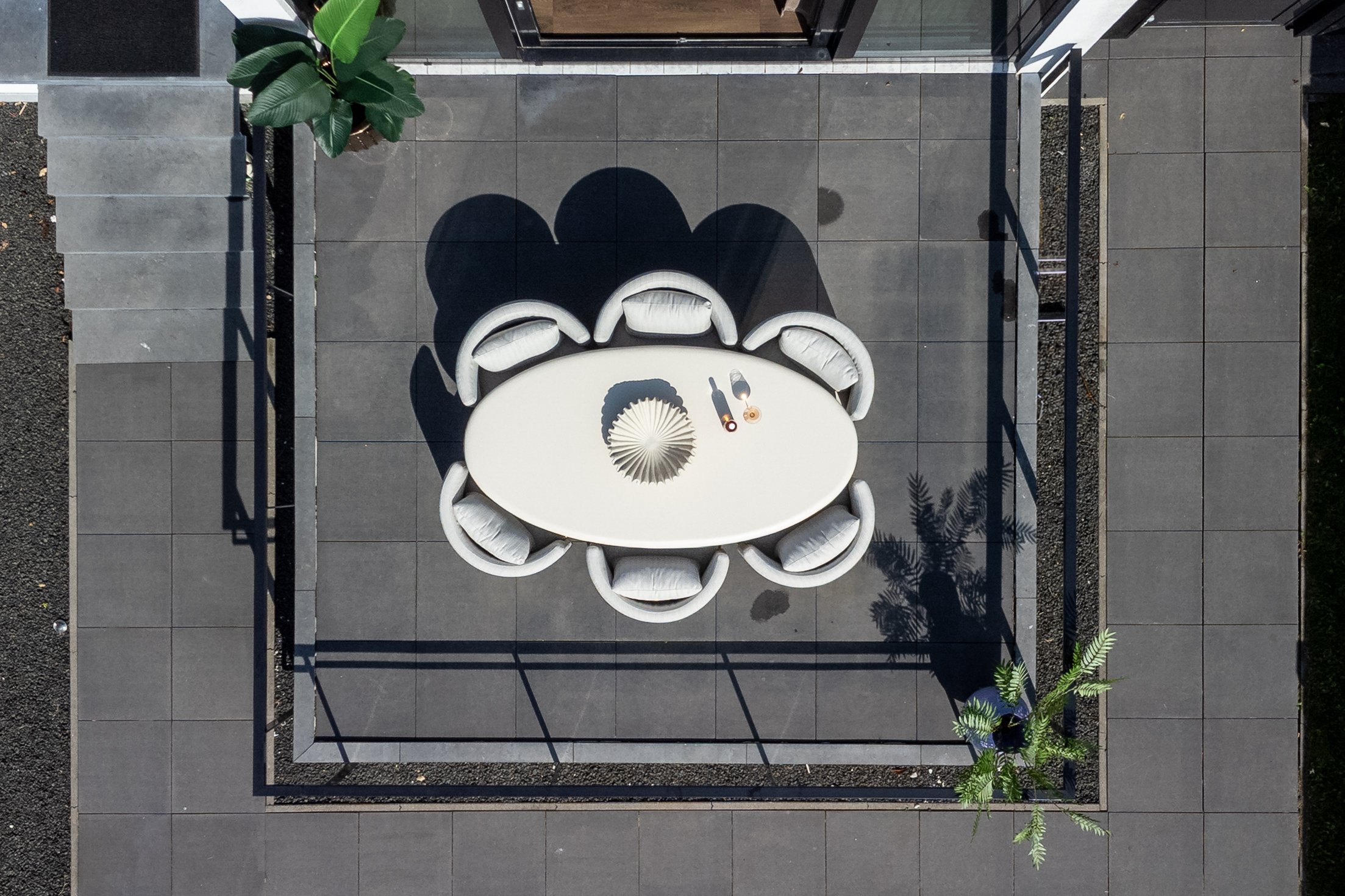 Compacte buitenruimte van bovenaf gezien met een ovale tafel en zes ronde stoelen op een grijze tegelvloer