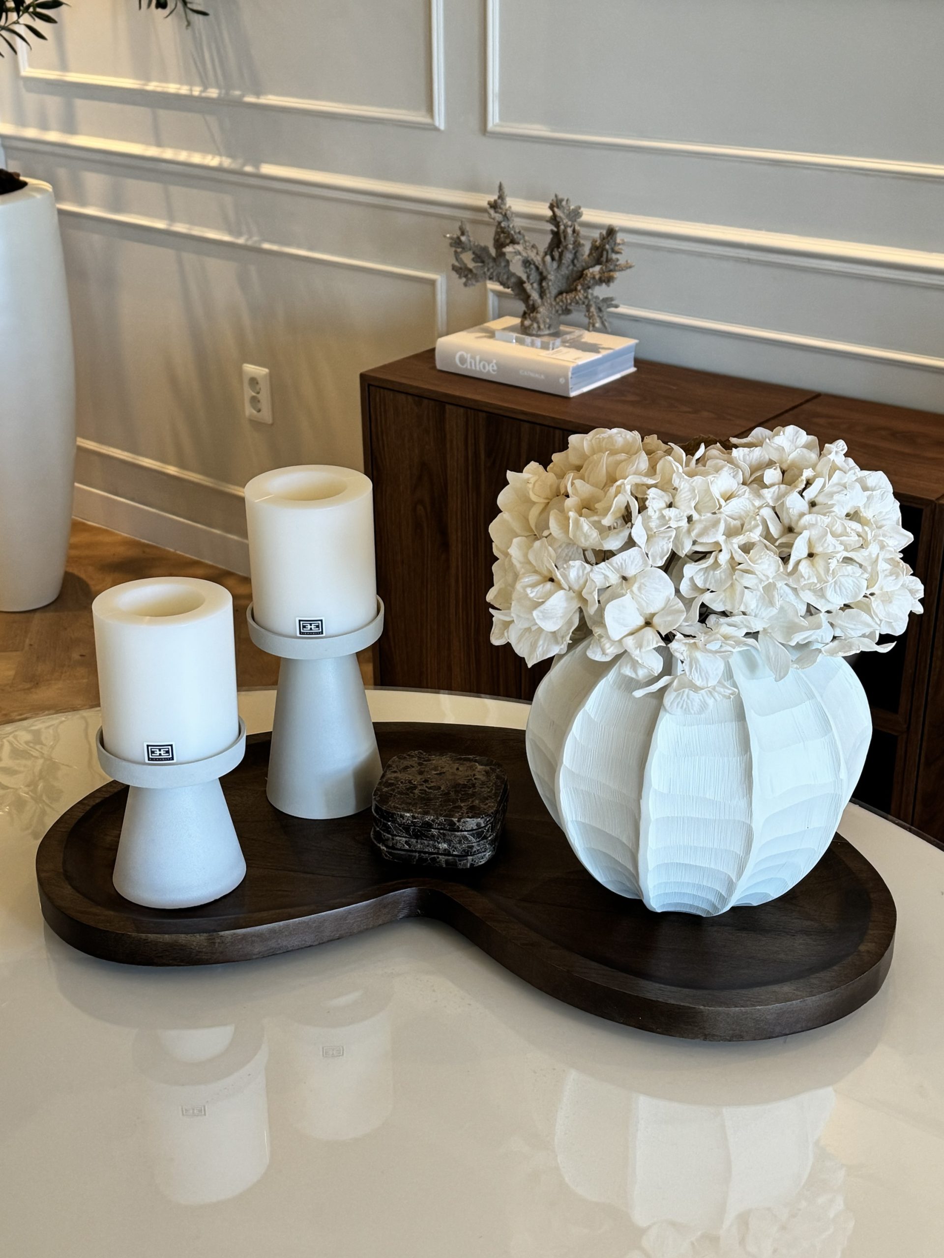 Donker houten dienblad met twee witte kaarshouders, marmeren onderzetters en een witte vaas met witte hortensia's