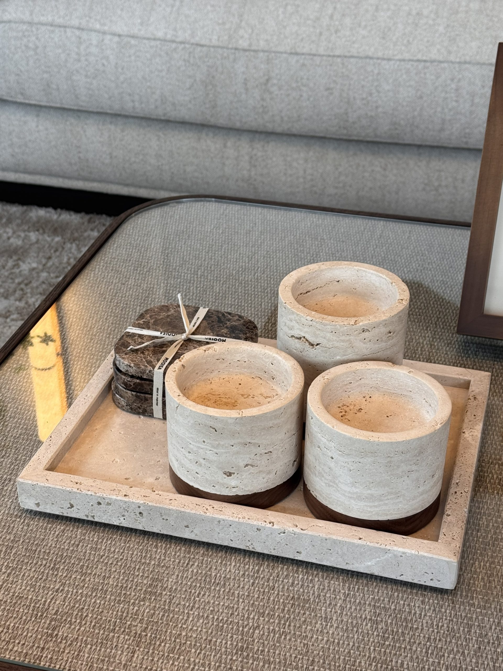Travertine dienblad met drie ronde travertin potjes en een setje bruine marmeren onderzetters op een salontafel